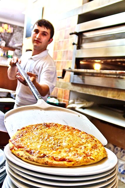 Pizzaiolo holt eine frisch gebackene Pizza aus dem Steinofen